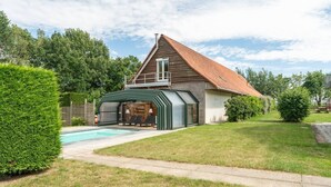 A house with a swimming pool, a covered patio, and a well-maintained lawn.