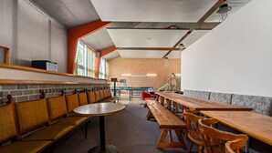 A cafeteria with long wooden tables and benches, a round table in the center, and a brick wall in the background.