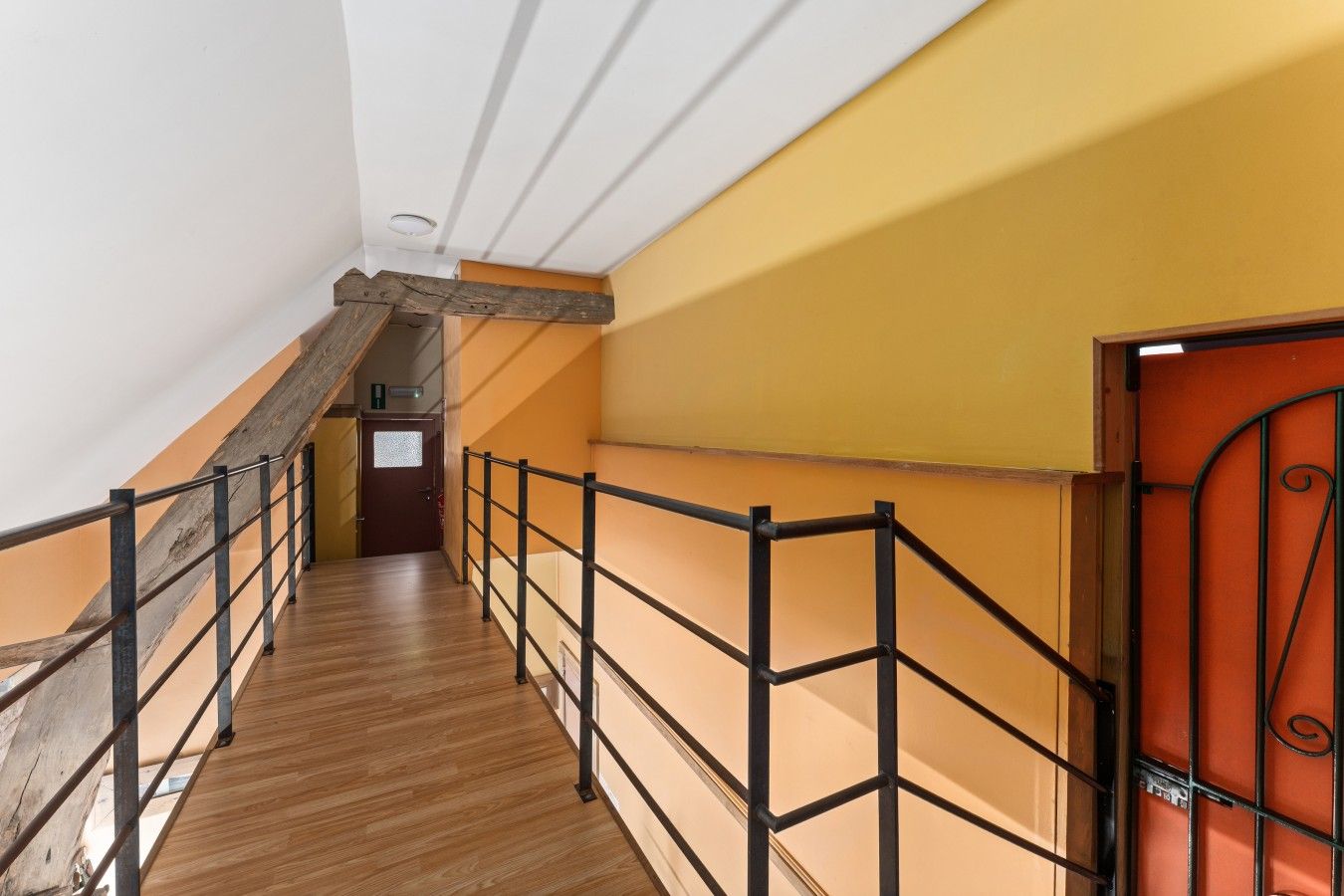 Una escalera de madera con barandillas de metal que conduce a una puerta con un portón metálico decorativo.