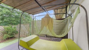A hammock chair under a metal frame with a net canopy, set on a wooden deck with a wooden fence and greenery in the background.