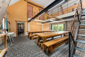 Een restaurantruimte met meerdere niveaus, houten tafels en banken, een stenen vloer en een trap.