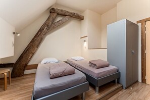 Een slaapkamer met twee bedden, een kledingkast en een houten balkenstructuur.