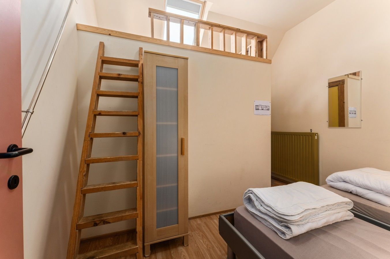 Ein Zimmer mit einer Holzleiter, die zu einem Schlafnest führt, einem Bett mit weißer Bettwäsche, einem Heizkörper und einem Fenster mit Blick.