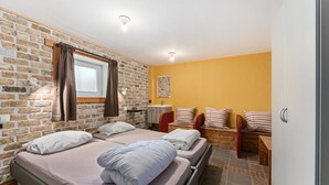 Ein Schlafzimmer mit Backsteinwand, einem Fenster mit Vorhängen, einem Bett mit Kissen, einem Nachttisch und einem roten Sessel.
