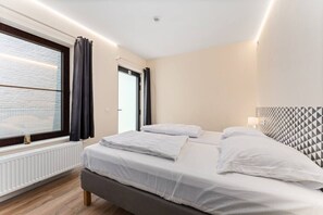 Ein modernes Hotelzimmer mit einem großen Bett, einem Fenster mit Vorhängen, einem Heizkörper und einem Kopfteil mit geometrischem Muster.