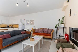 A modern living room with a sofa, a coffee table, and a television. - Barbara`s Guesthouse (Poperinge)