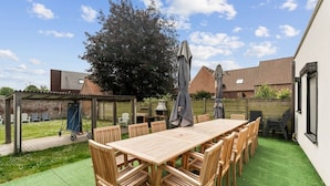 Un patio con una mesa y sillas de madera, rodeado de césped verde y un muro de ladrillo.