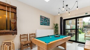Una mesa de billar en una habitación con vistas al exterior, sillas de madera y un cuadro en la pared.