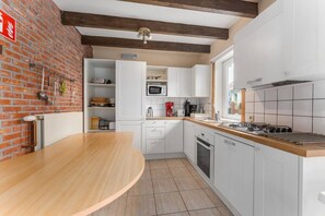 A modern kitchen with white cabinets, a wooden countertop, and a brick wall.