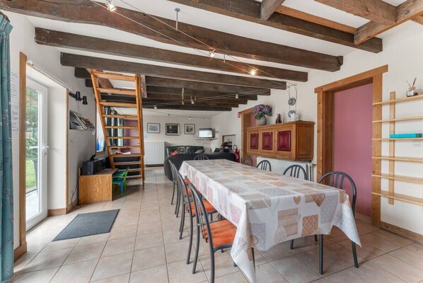 A dining area with a long table, chairs, a ladder, and a wooden cabinet.