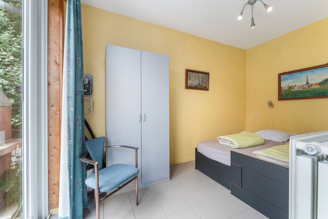 Una camera da letto con un letto, una sedia, un armadio e un quadro appeso al muro.