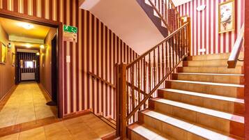 A hotel hallway with a wooden staircase and striped wallpaper.