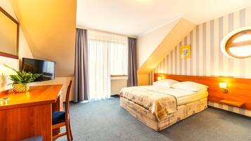 A hotel room with a bed, a desk with a television, a chair, a window with curtains, and a wall with a striped pattern.