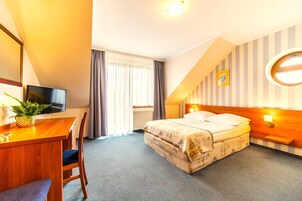 Habitación de hotel con cama, escritorio con televisor, una silla, ventana con cortinas y pared con diseño a rayas.
