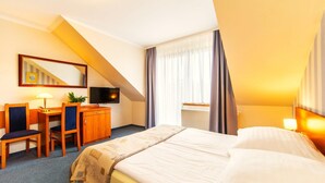 Quarto de hotel com cama, escrivaninha, cadeira, televisão e janela com cortinas.
