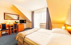 Ein Hotelzimmer mit einem Bett, einem Schreibtisch, einem Sessel, einem Fernseher und einem fenster mit Vorhängen.