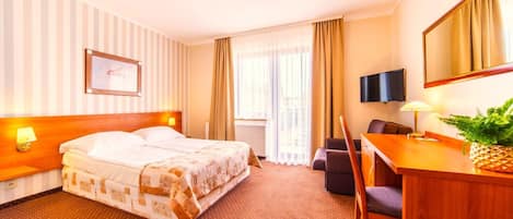 A hotel room with a bed, a desk, a chair, a TV, and a window with curtains.