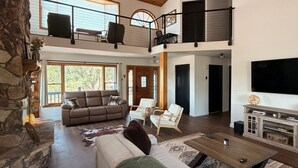 A spacious living area with a high ceiling, a fireplace, a large sofa, a coffee table, and a television. - The Pine Loft, Spacious Mountain Escape in Payson (Payson)