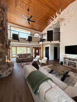 A spacious living area with a high ceiling, a fireplace, a large sofa, a coffee table, and a television. - The Pine Loft, Spacious Mountain Escape in Payson (Payson)