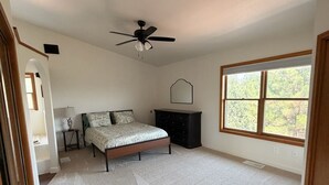 A bedroom with a bed, a ceiling fan, a dresser, a window, and a door. - The Pine Loft, Spacious Mountain Escape in Payson (Payson)
