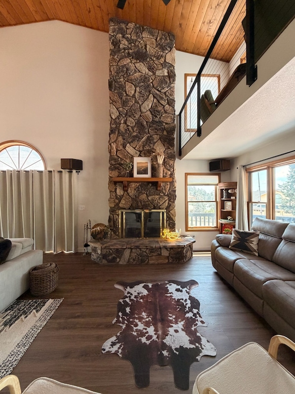 A spacious living room with a stone fireplace, a leather sofa, and a cowhide rug.