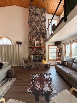 A spacious living room with a stone fireplace, a leather sofa, and a cowhide rug. - The Pine Loft, Spacious Mountain Escape in Payson (Payson)
