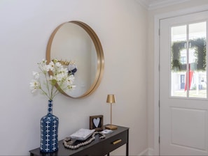 A room with a round mirror, a vase with flowers, a lamp, a small table with a picture frame and a heart-shaped object, and a door with a view of greenery outside. - Rebel'ado-Colorado Roots-Oxford Style! 3 King Ensuites -Sleeps 8 (Oxford)