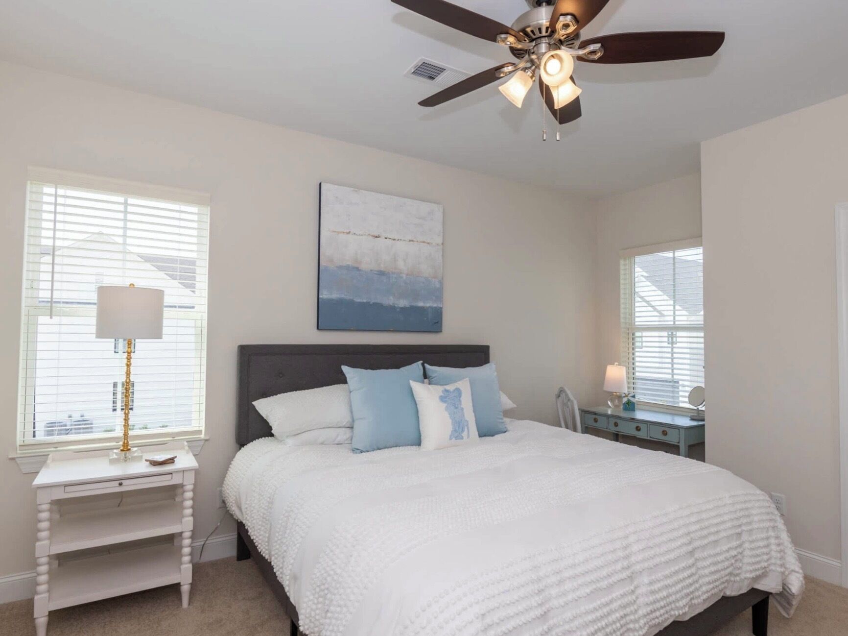 A bedroom with a bed, a nightstand, a desk, a ceiling fan, and a window with blinds.