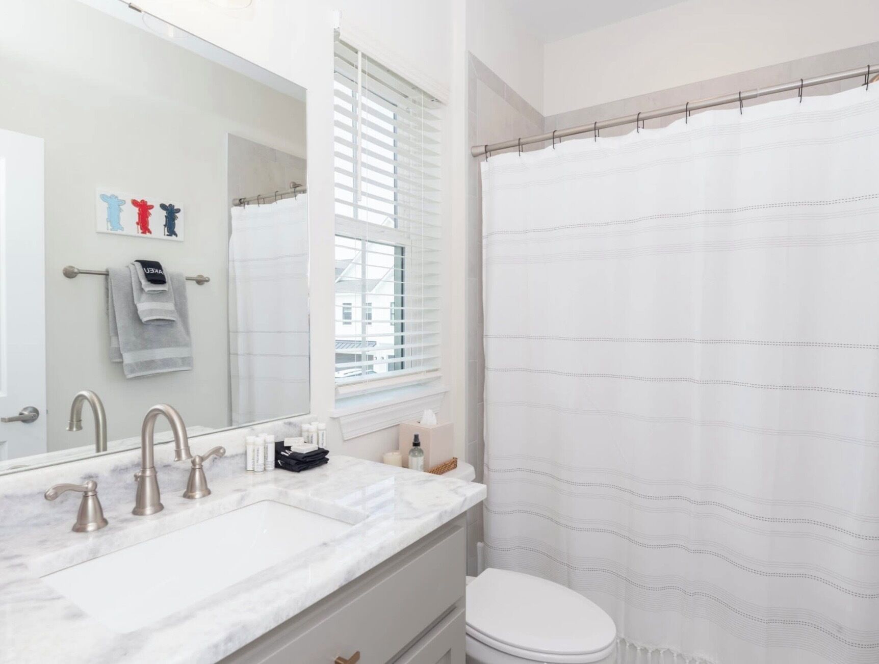 A bathroom with a white sink, two faucets, a mirror, a window with blinds, and a white toilet.