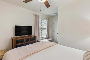 A bedroom with a bed, a television on a wooden dresser, a window with blinds, and a door. - Stillwater Cottage - Dock + Fishing (Brunswick)