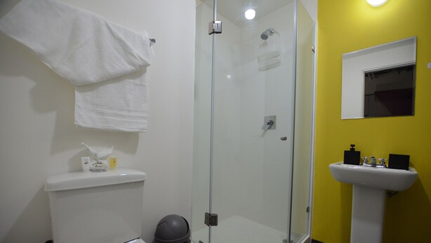 Une salle de bain avec une douche à parois de verre, des toilettes blanches, un lavabo et un mur jaune.