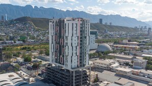 Un immeuble de grande hauteur, composé de plusieurs étages, entouré d’un paysage urbain et avec des montagnes en arrière-plan.