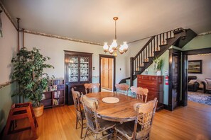A dining area with a wooden table and chairs, a chandelier, and a staircase leading to another level.