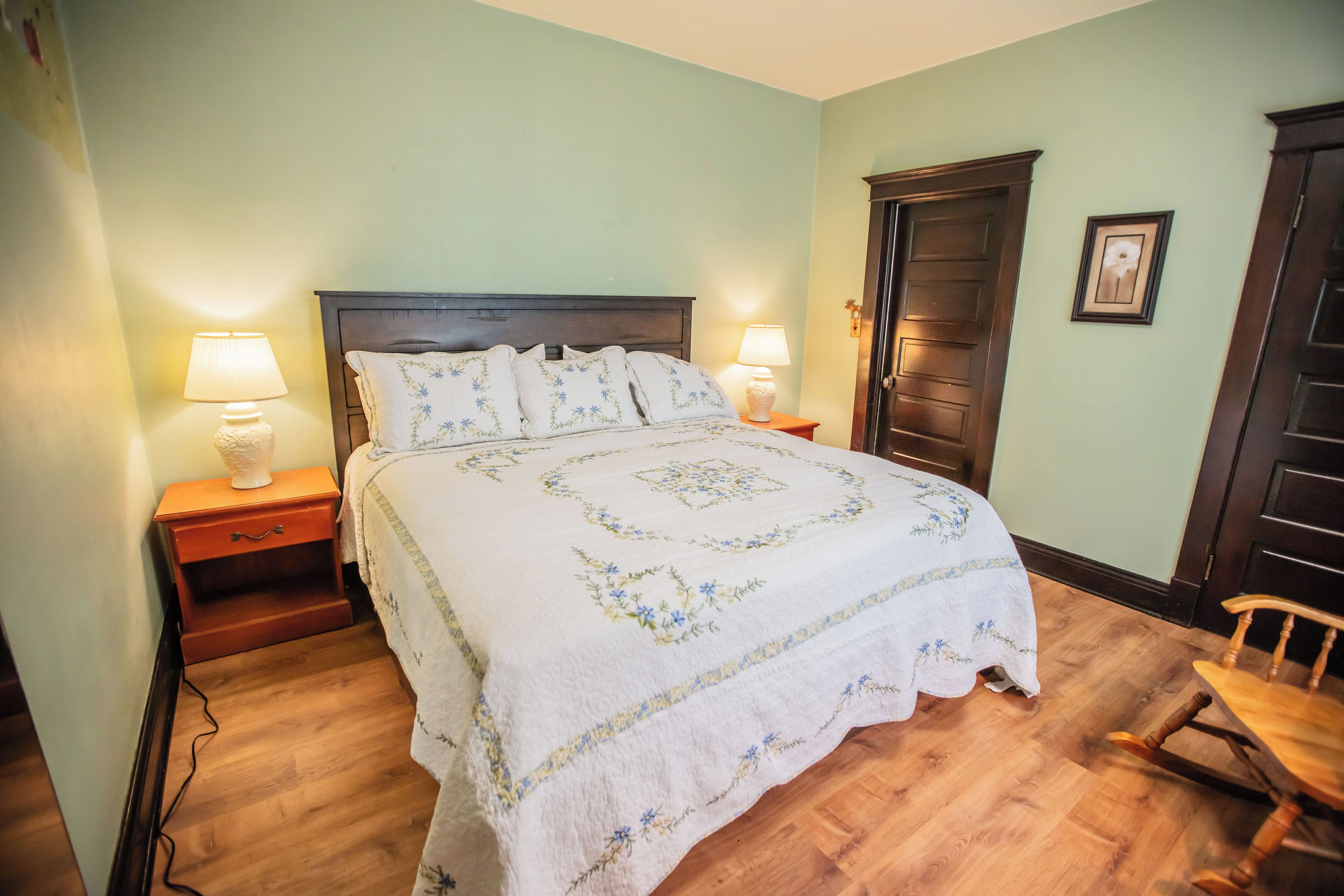 A bedroom with a bed, two bedside tables with lamps, a wooden door, and a chair.