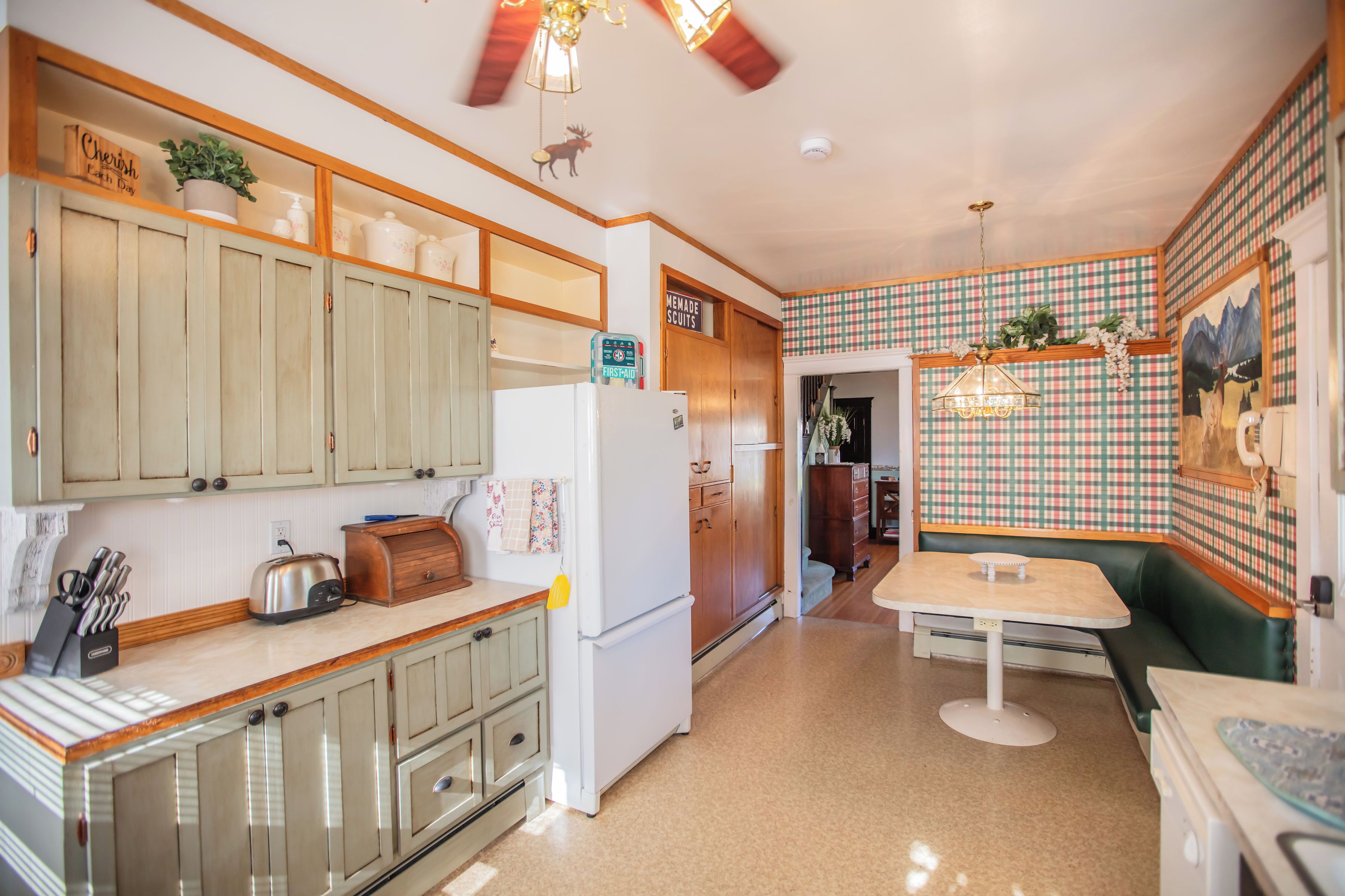 A kitchen with wooden cabinets, a refrigerator, a toaster, and a dining area with a table and bench.