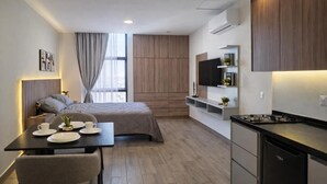 A modern hotel room with a bed, a dining area with a table and chairs, a kitchen with a stove, and a TV mounted on the wall. - Colonia10 by tuhost (Monterrey)