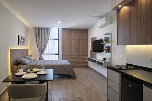 Una habitación de hotel moderna con una cama, un comedor con mesa y sillas, una cocina con estufa y un televisor montado en la pared.