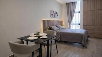Una habitación de hotel moderna con una cama, una mesa de comedor con sillas y una pequeña mesa con una planta.