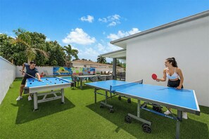Ein Außenbereich mit zwei Tischtennisplatten, einem Billardtisch und einer Lounge mit Wandgemälde.