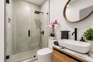 Ein modernes Badezimmer mit einer gläsernen Duschkabine, einem weißen Waschbecken und einem Holz-Badmöbel.