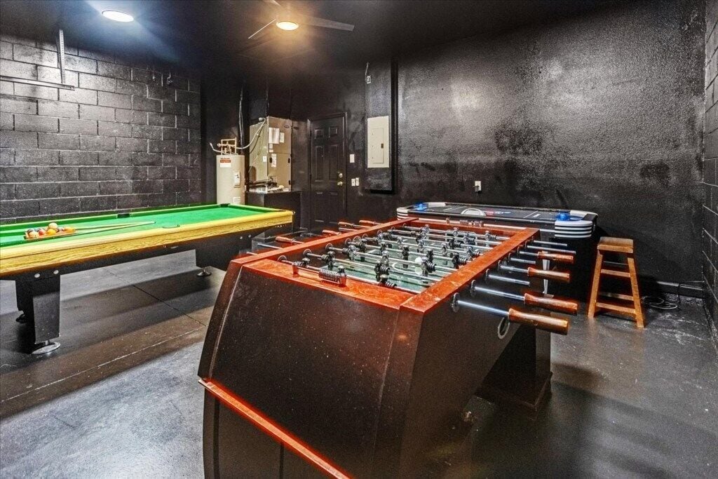 A billiards table, a foosball table, and a pool table in a room with brick walls and a dark floor.