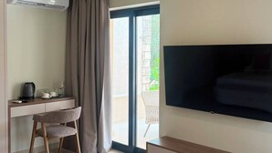 Una habitación moderna con una televisión de pantalla plana montada en la pared, un escritorio con una silla, cafetera y una puerta corrediza de vidrio que da a un área exterior.