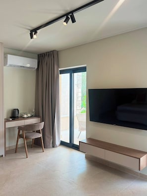 A modern room with a flat-screen TV mounted on the wall, a desk with a chair, a coffee maker, and a sliding glass door leading to an outdoor area.