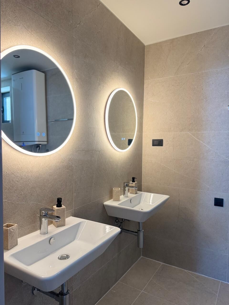 Un baño moderno con dos lavamanos, un espejo grande con luz y un dispensador de toallas.