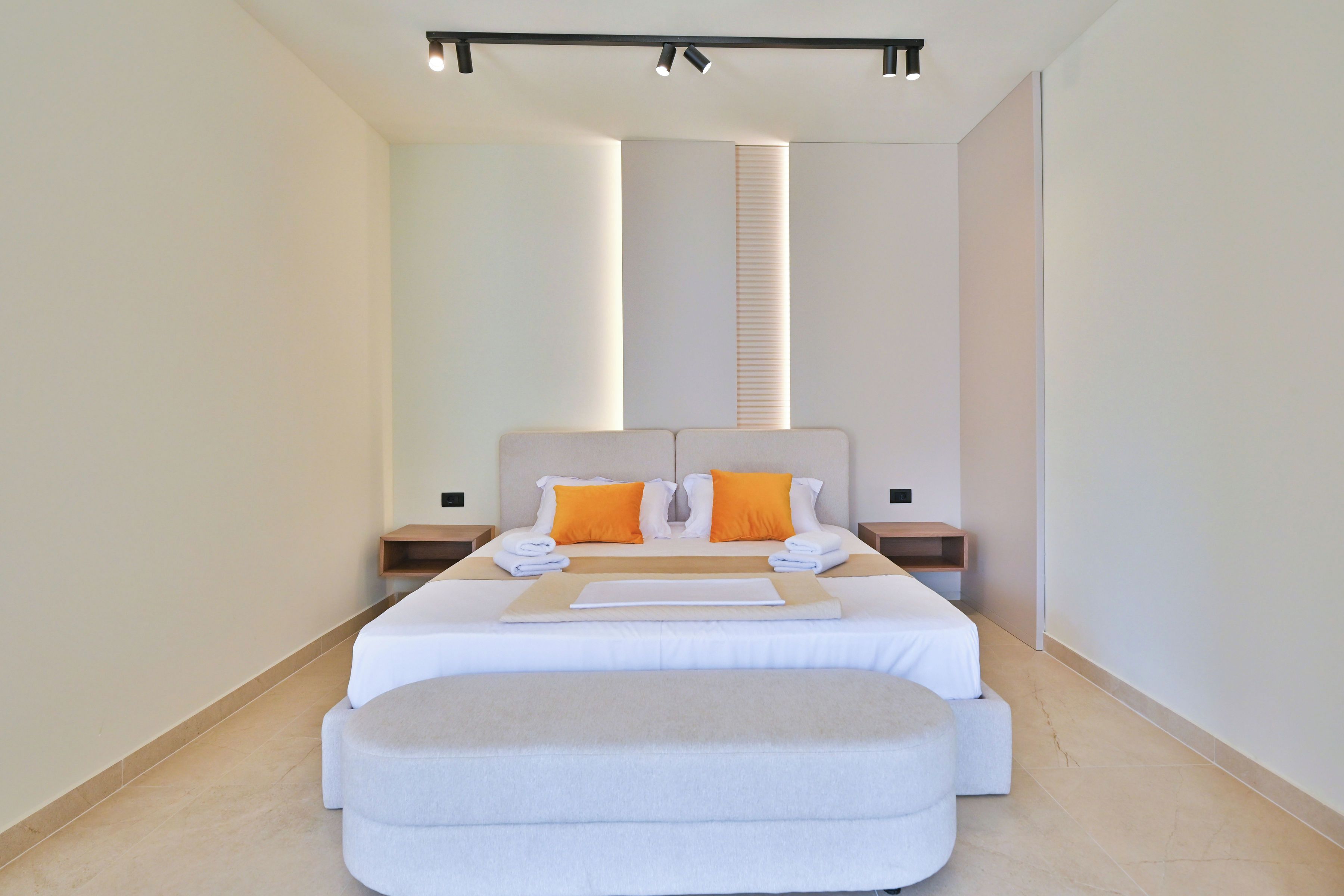 Une chambre d’hôtel moderne avec un grand lit, deux tables de chevet, une petite table et un banc intégré.