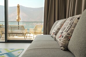 Un salón moderno con un sofá, dos sillas de mimbre y vistas al mar y a las montañas a través de grandes ventanales.