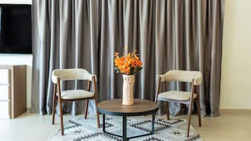 Une pièce avec deux chaises, une petite table, un vase de fleurs et un téléviseur placé devant un rideau.