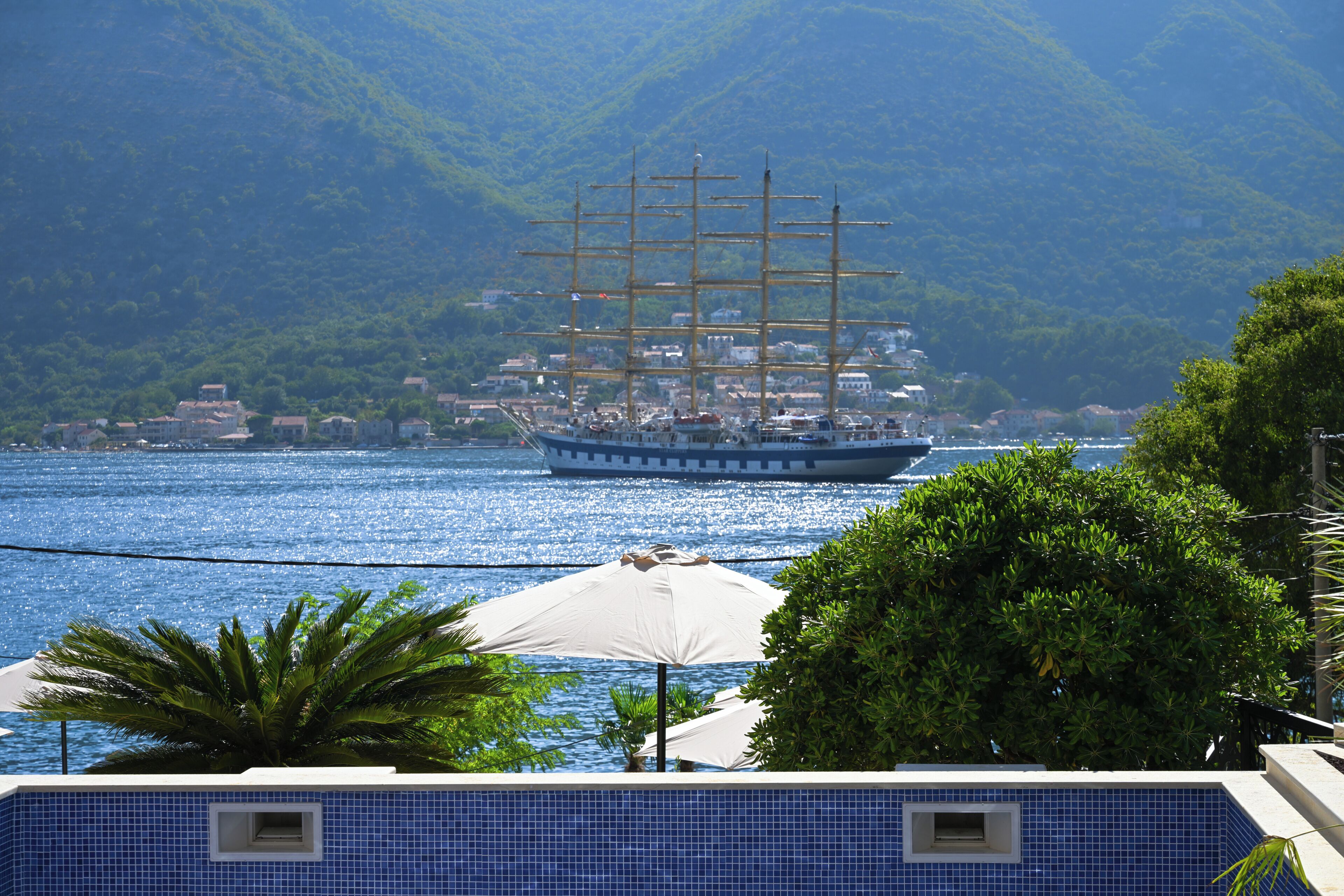 A coastal scene with a large sailing ship, a swimming pool, and a mountainous backdrop.