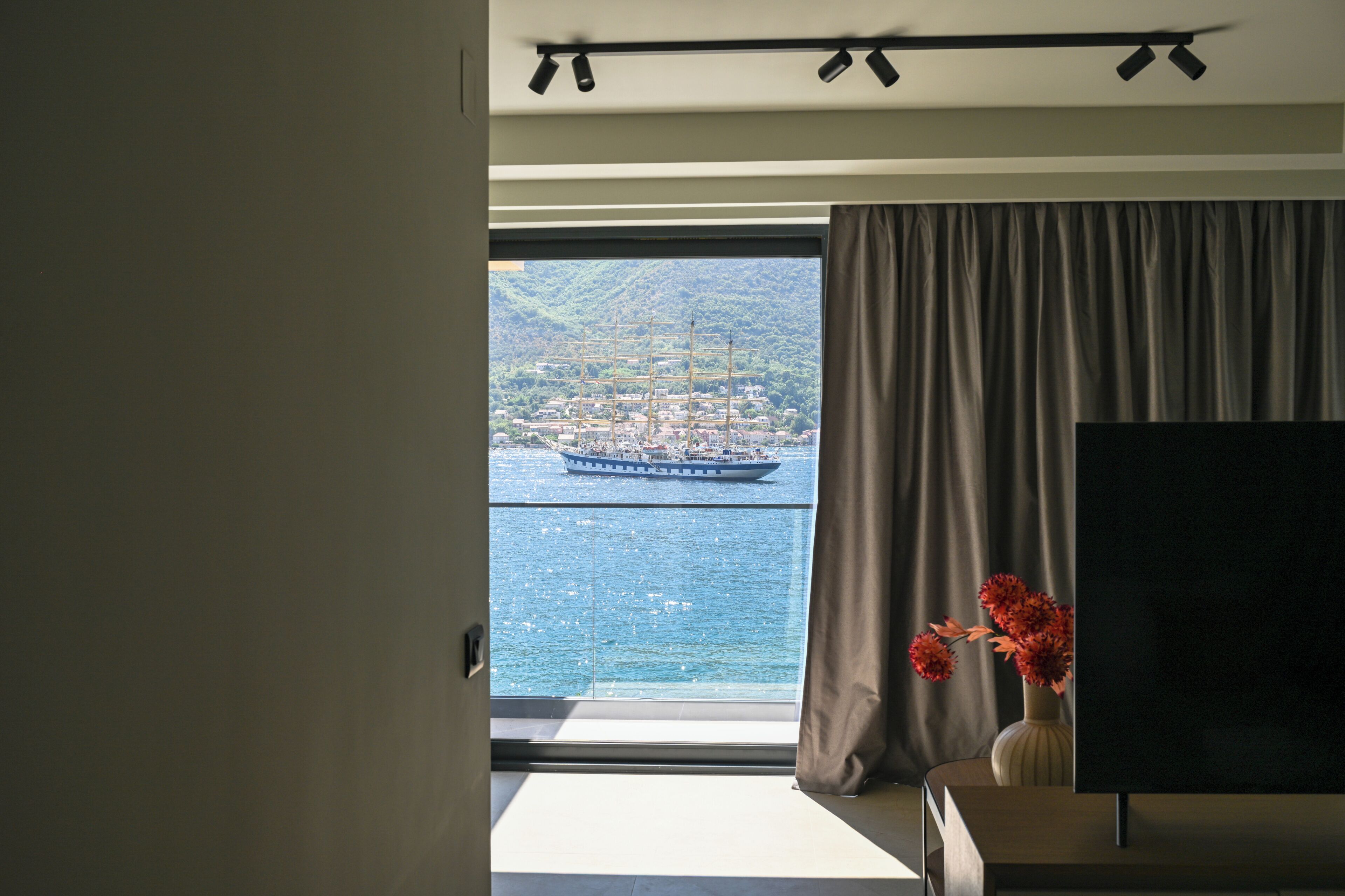 Una habitación con un ventanal grande, un televisor de pantalla plana y un florero con flores.