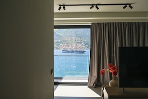 A room with a large window, a flat-screen TV, and a vase with flowers.